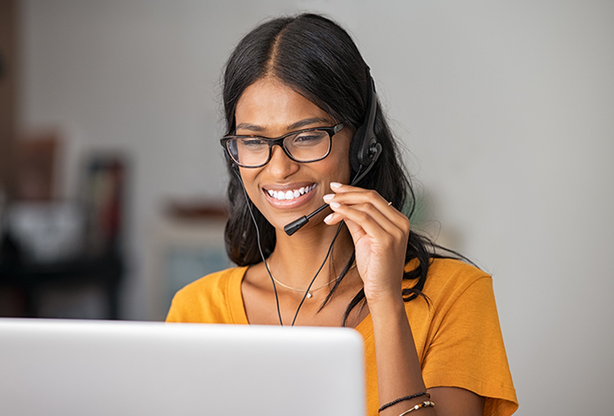 Portrait of cheerful indian woman in smart working from home. Beautiful middle eastern girl working as customer service representative with laptop. Smiling young woman at home with headset doing video call and smiling.